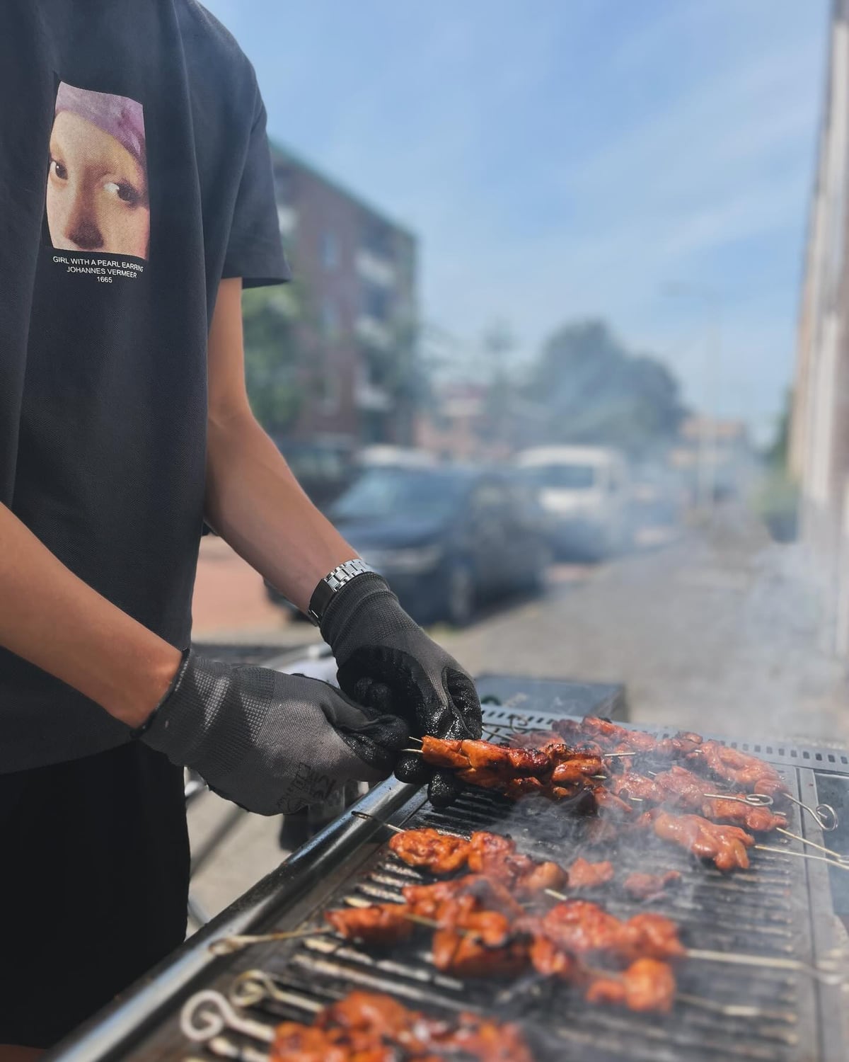 Kipsaté op de grill, een medewerker in zwarte handschoenen draait de spiesen om